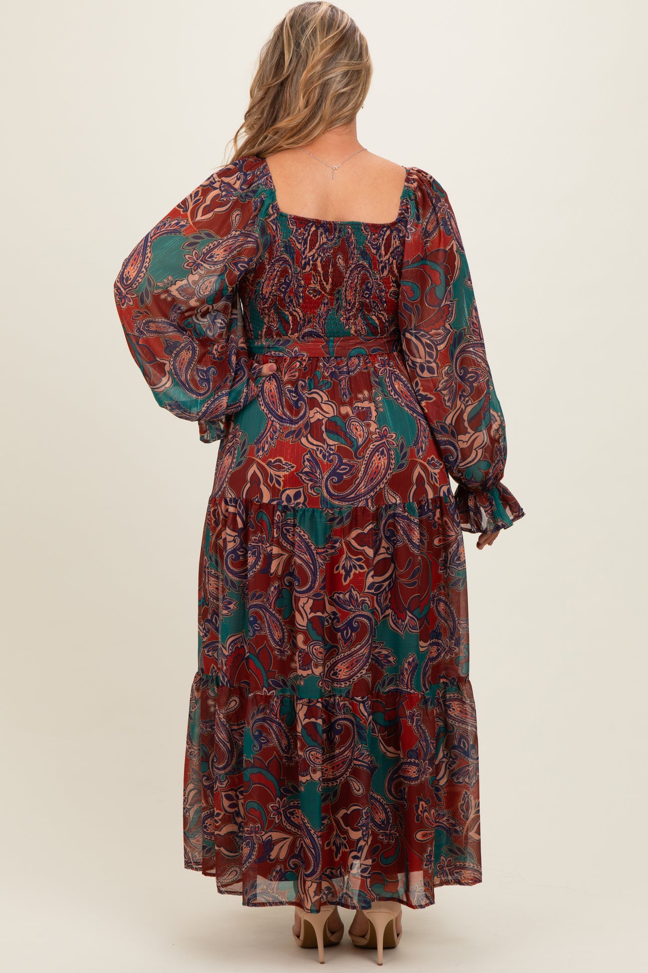 woman wearing a long sleeve red and green paisley print maternity maxi dress with a tiered hemline and a flowy silhouette