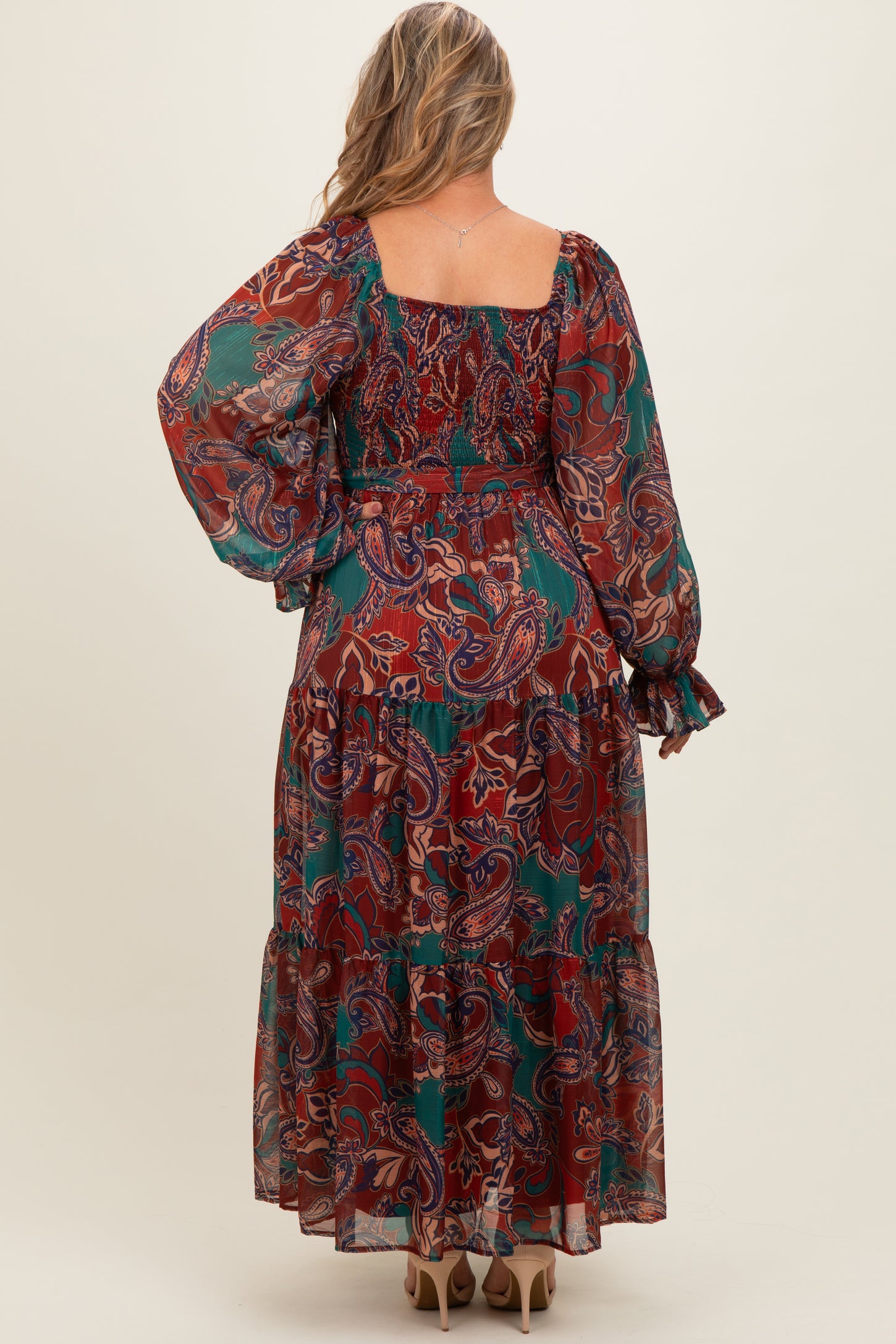 woman wearing a long sleeve red and green paisley print maternity maxi dress with a tiered hemline and a flowy silhouette