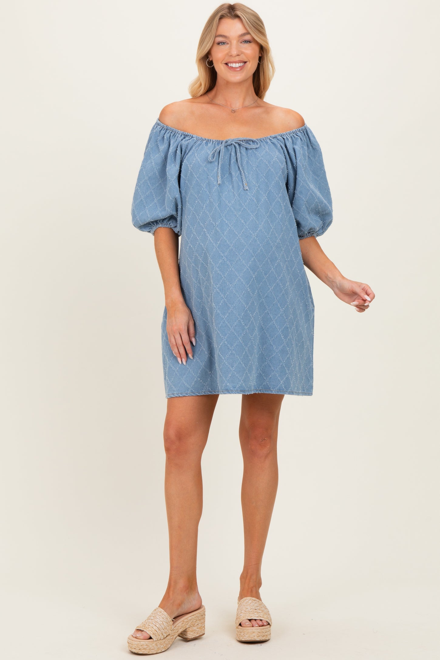 woman wearing a light blue off-the-shoulder maternity dress with puff sleeves and a tie detail