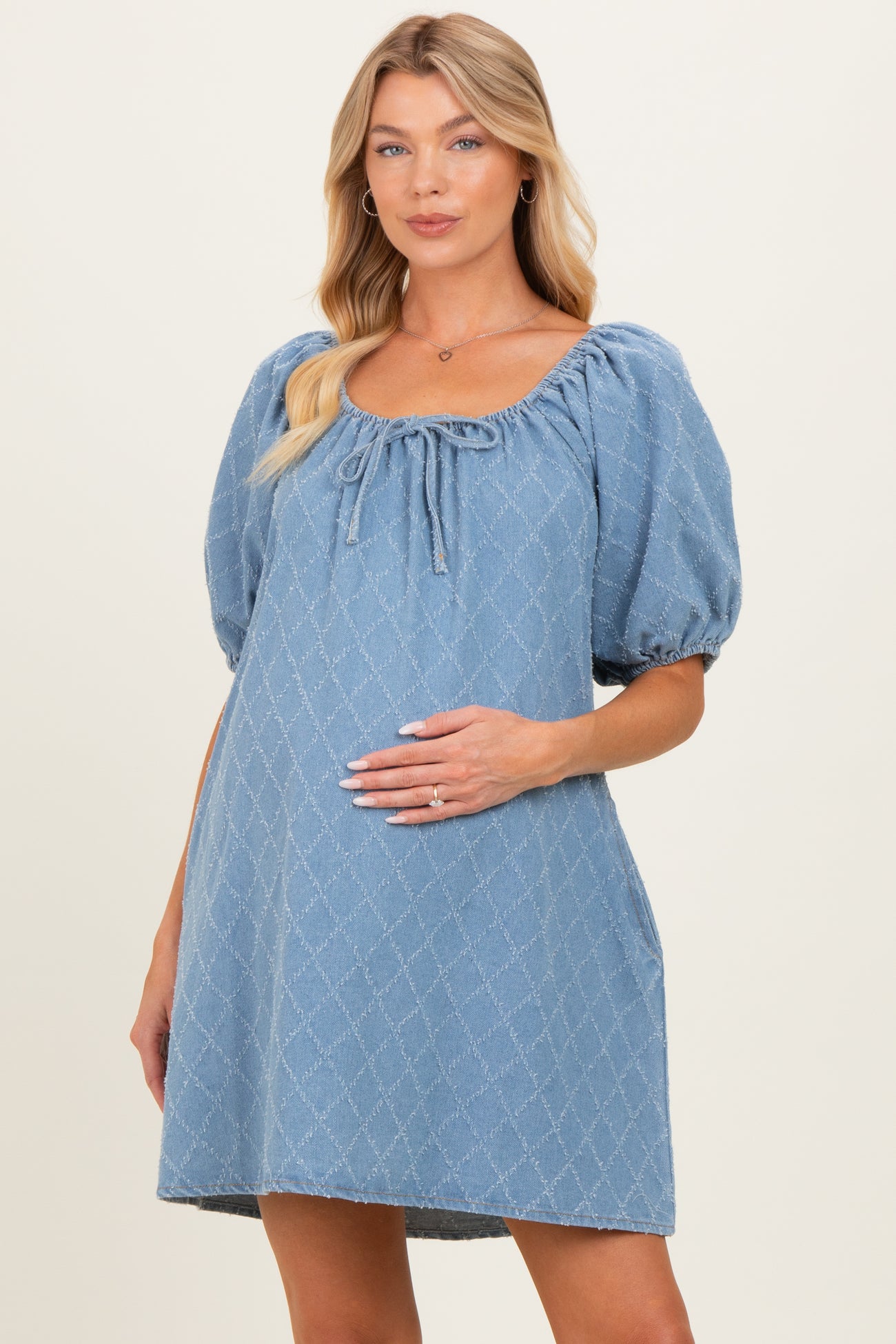 woman wearing a light blue short puff sleeve maternity dress with a scoop neckline and holding her baby bump