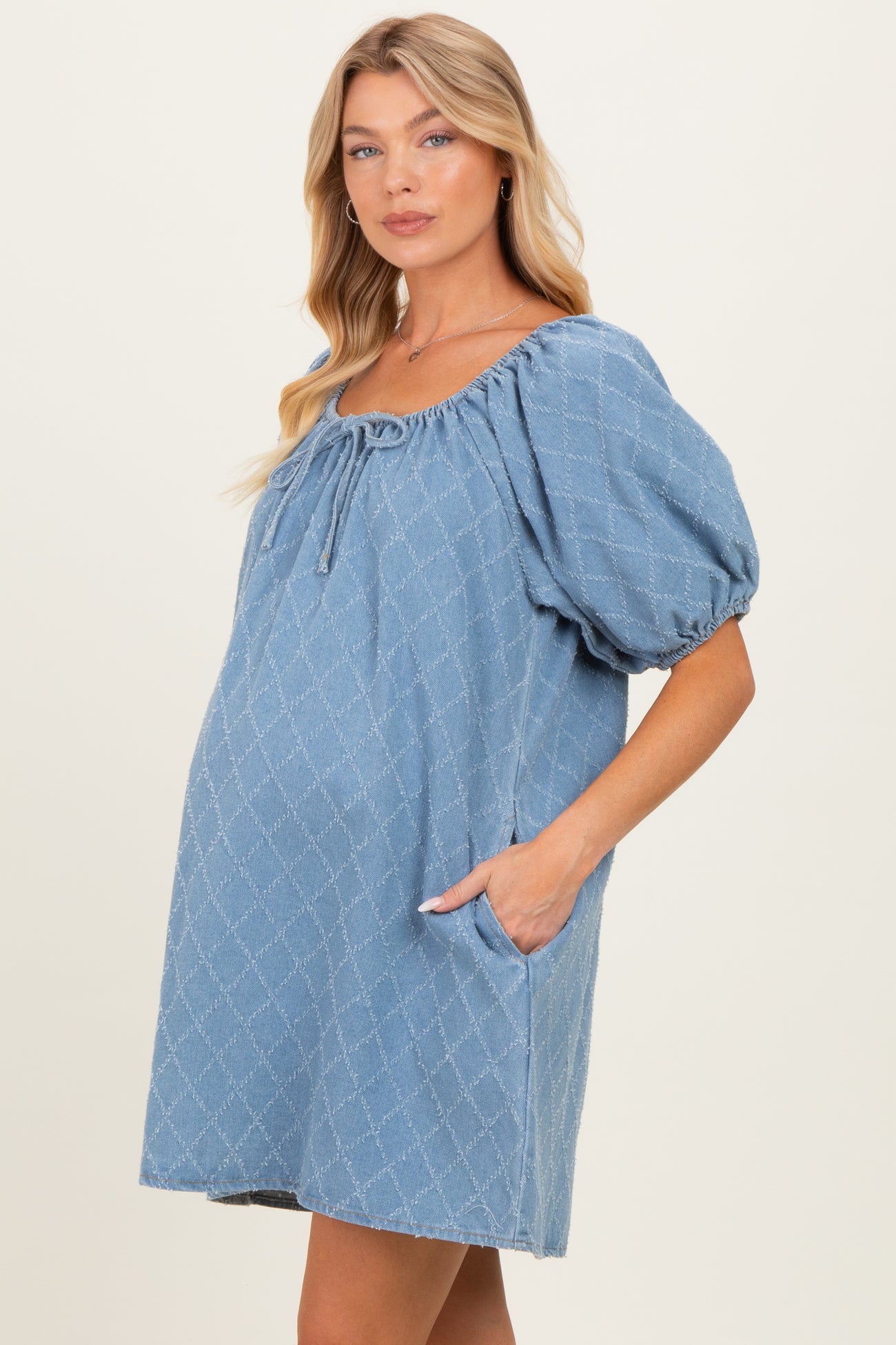 woman wearing a light blue maternity dress with puff sleeves and front pockets, showing her baby bump