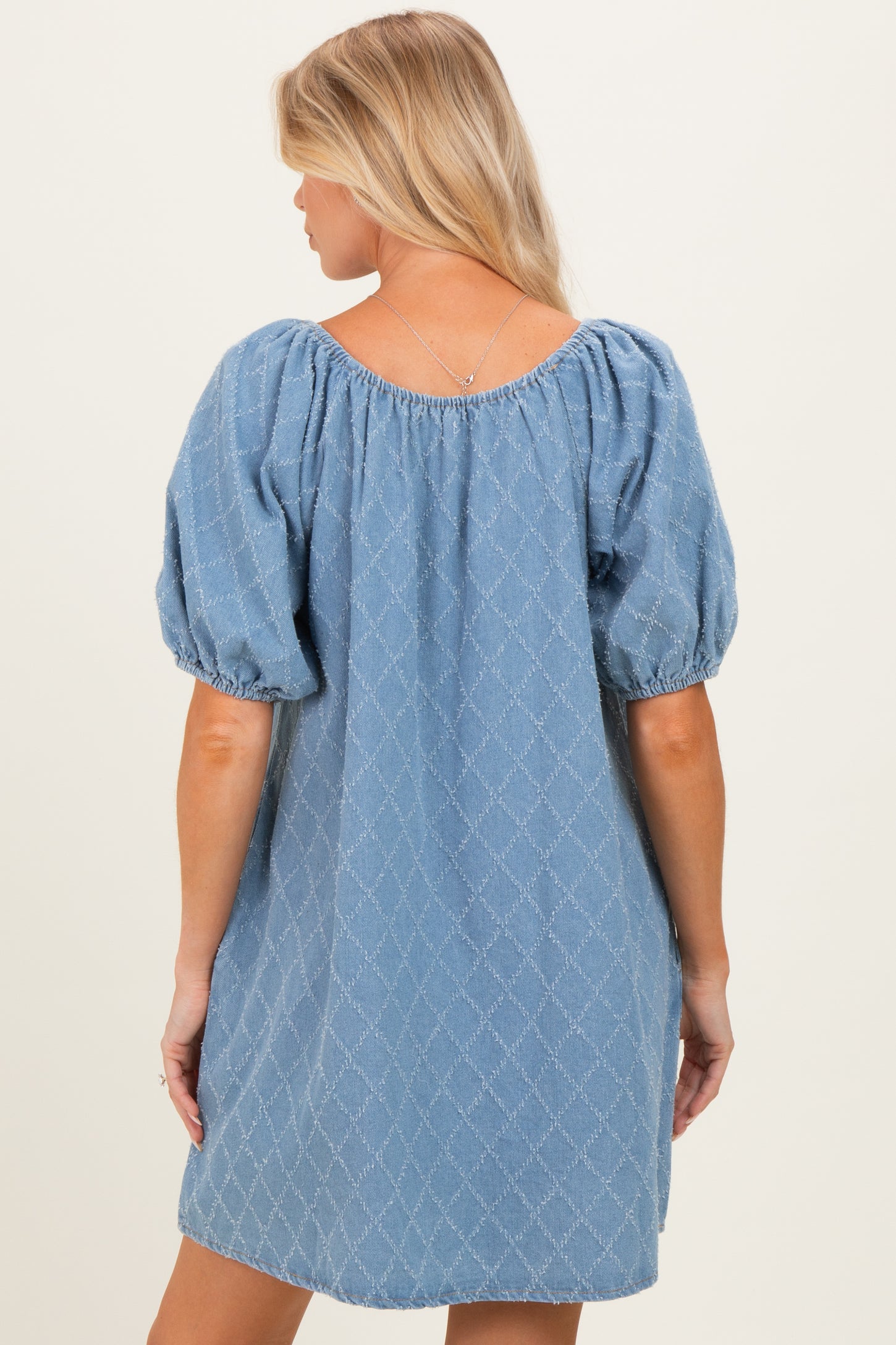 woman wearing a blue puff sleeve maternity dress with a diamond pattern, showing the back view