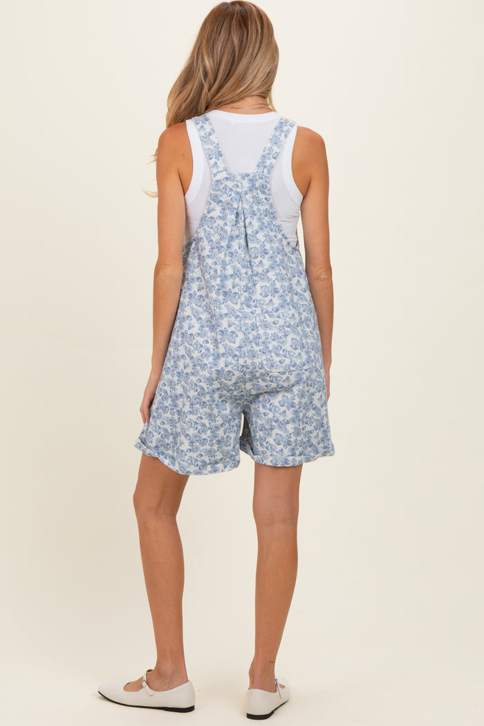 woman wearing a floral print blue maternity short overalls with a white tank top underneath and casual shoes
