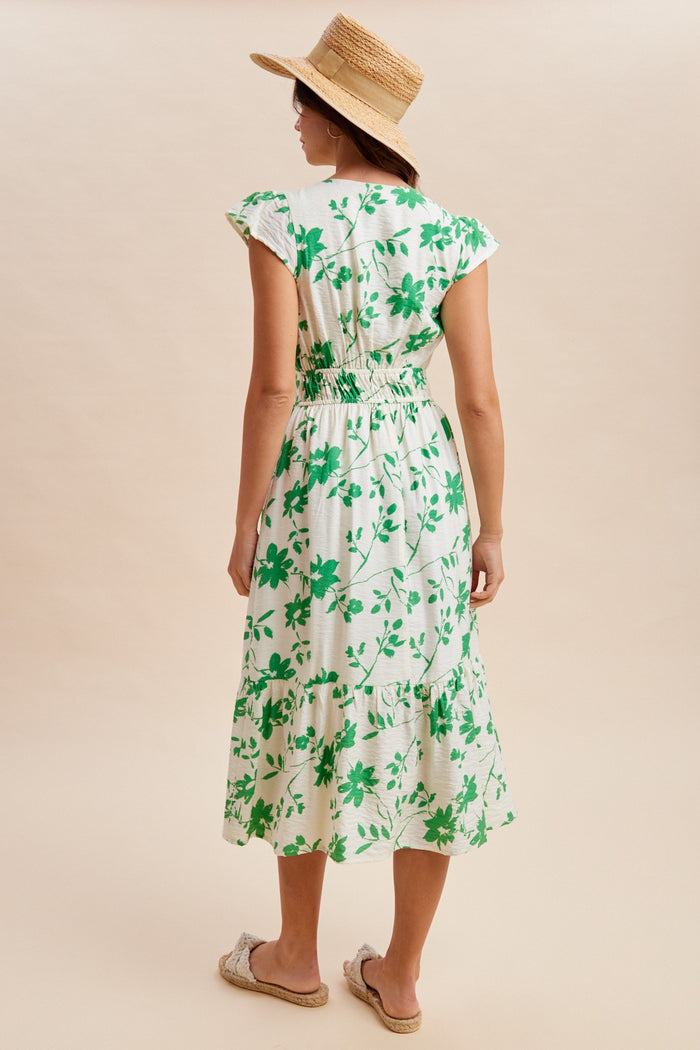 woman wearing a green floral midi dress with ruffled sleeves and smocked waist, standing with her back to the camera