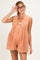 woman wearing a peach colored maternity romper with pleats and tie detail, smiling and adjusting her glasses
