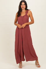 woman wearing a rust-colored sleeveless maxi dress with ruffle shoulders and wide-leg style