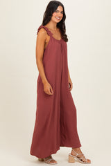 woman wearing a rust-colored maxi dress with ruffled straps and a flowing silhouette, standing sideways against a neutral background