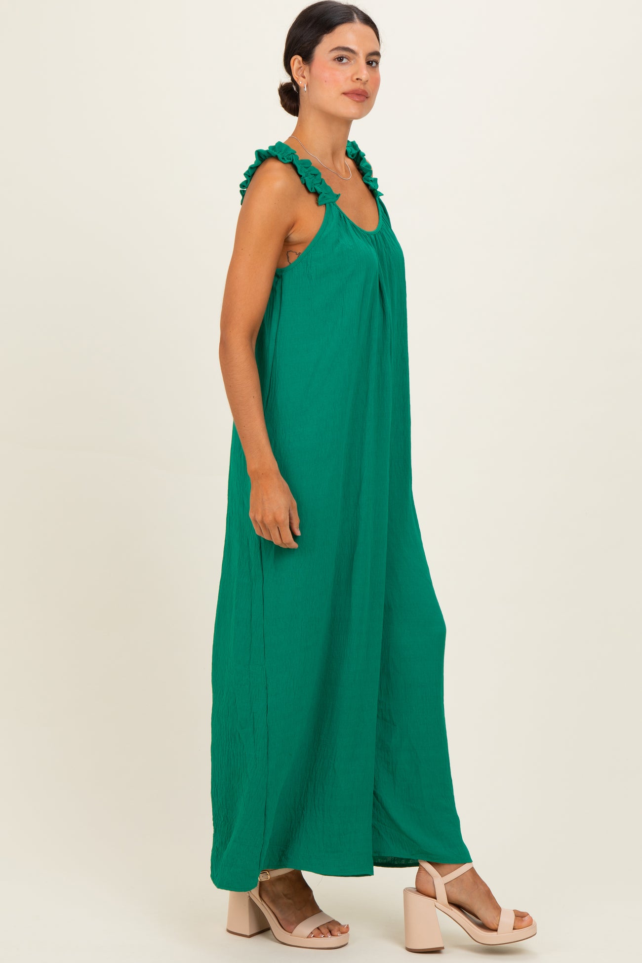 woman wearing a green sleeveless maxi dress with ruffled straps and standing in profile