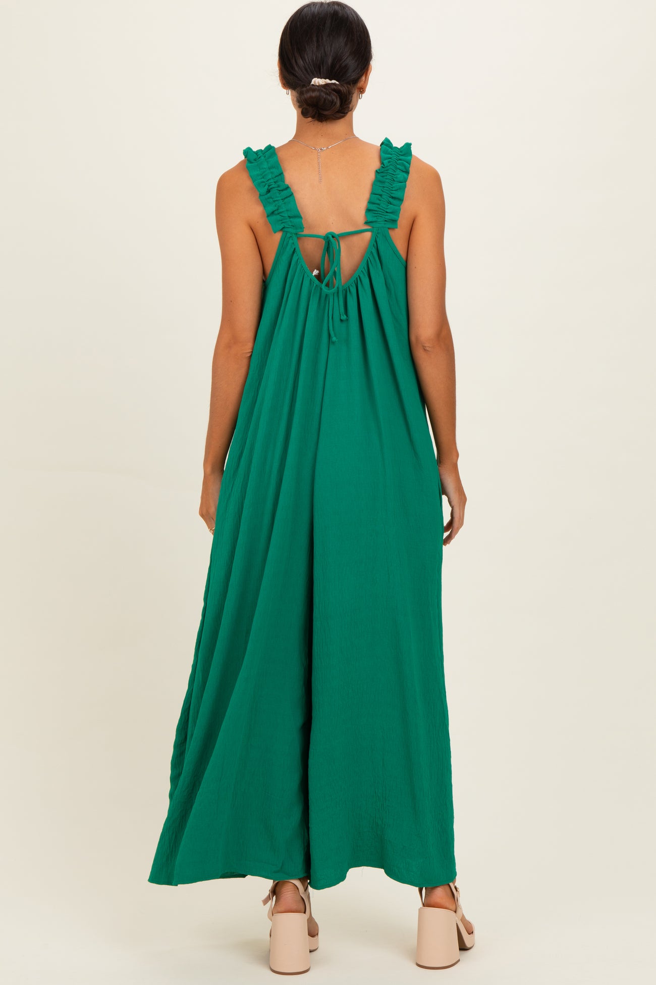 woman wearing a green sleeveless maxi dress with ruffle straps and an open back detail