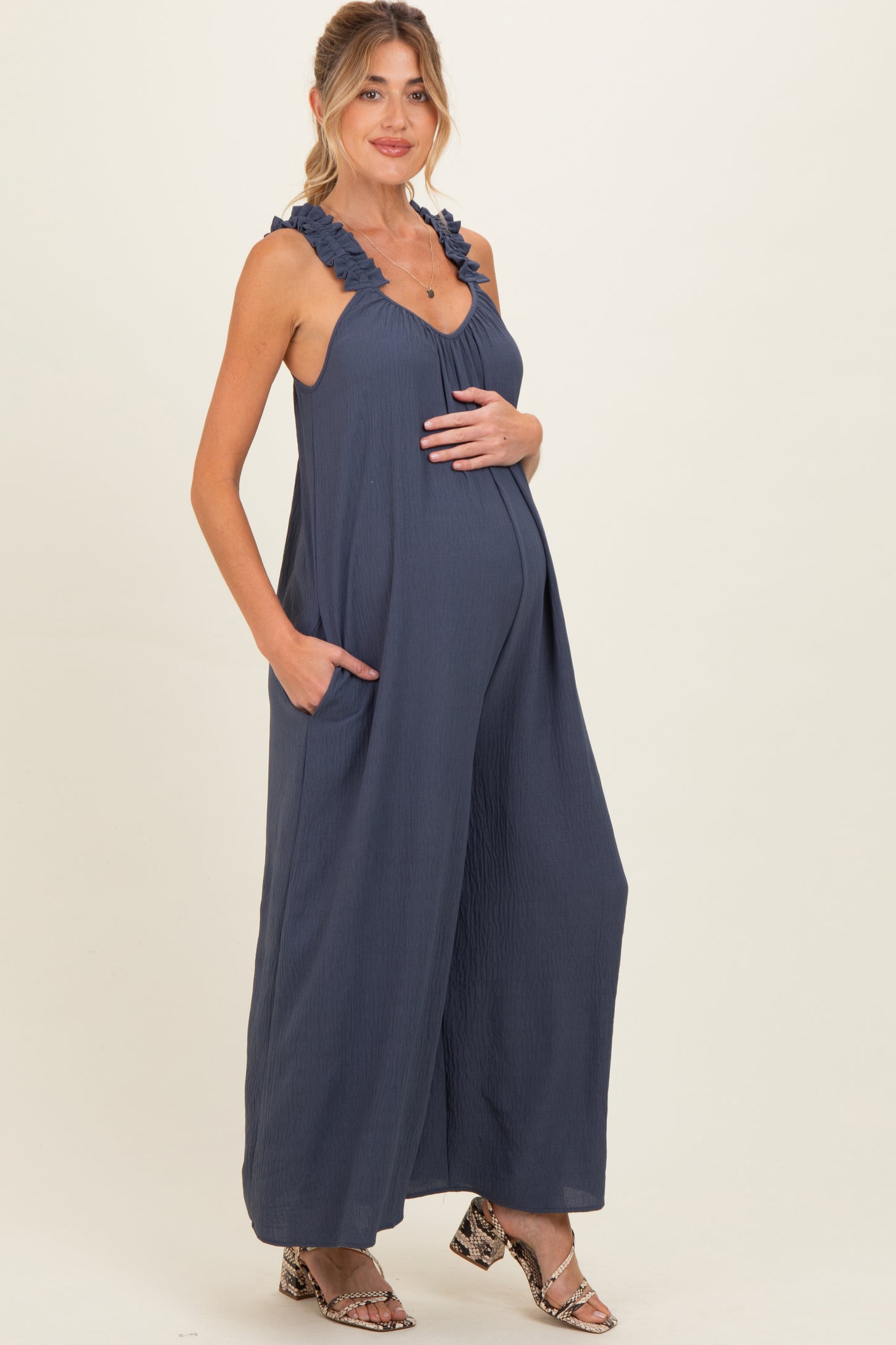 woman wearing a navy blue sleeveless maternity jumpsuit with ruffled straps and pockets, showing her baby bump