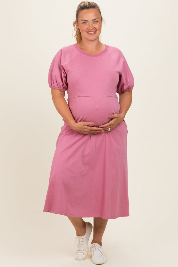 woman wearing a pink puff sleeve maternity dress and gently holding her baby bump