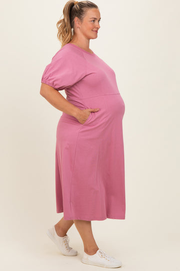 woman wearing a pink maternity plus midi dress with short sleeves and pockets, showing her baby bump