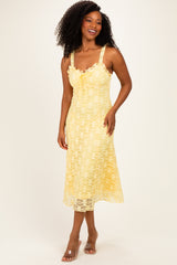 woman wearing a light yellow lace midi dress with thick straps and a bow tie detail at the bust