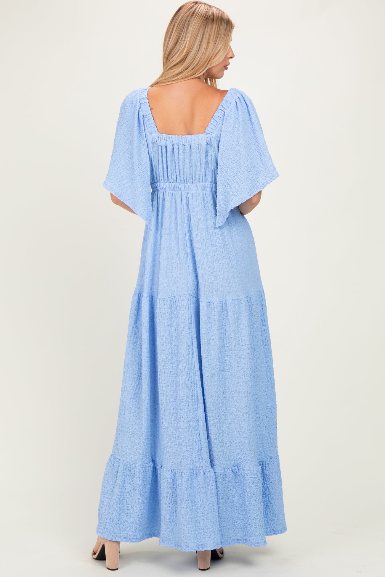 woman wearing a light blue maxi dress with short flutter sleeves and tiered ruffle hem, shown from the back