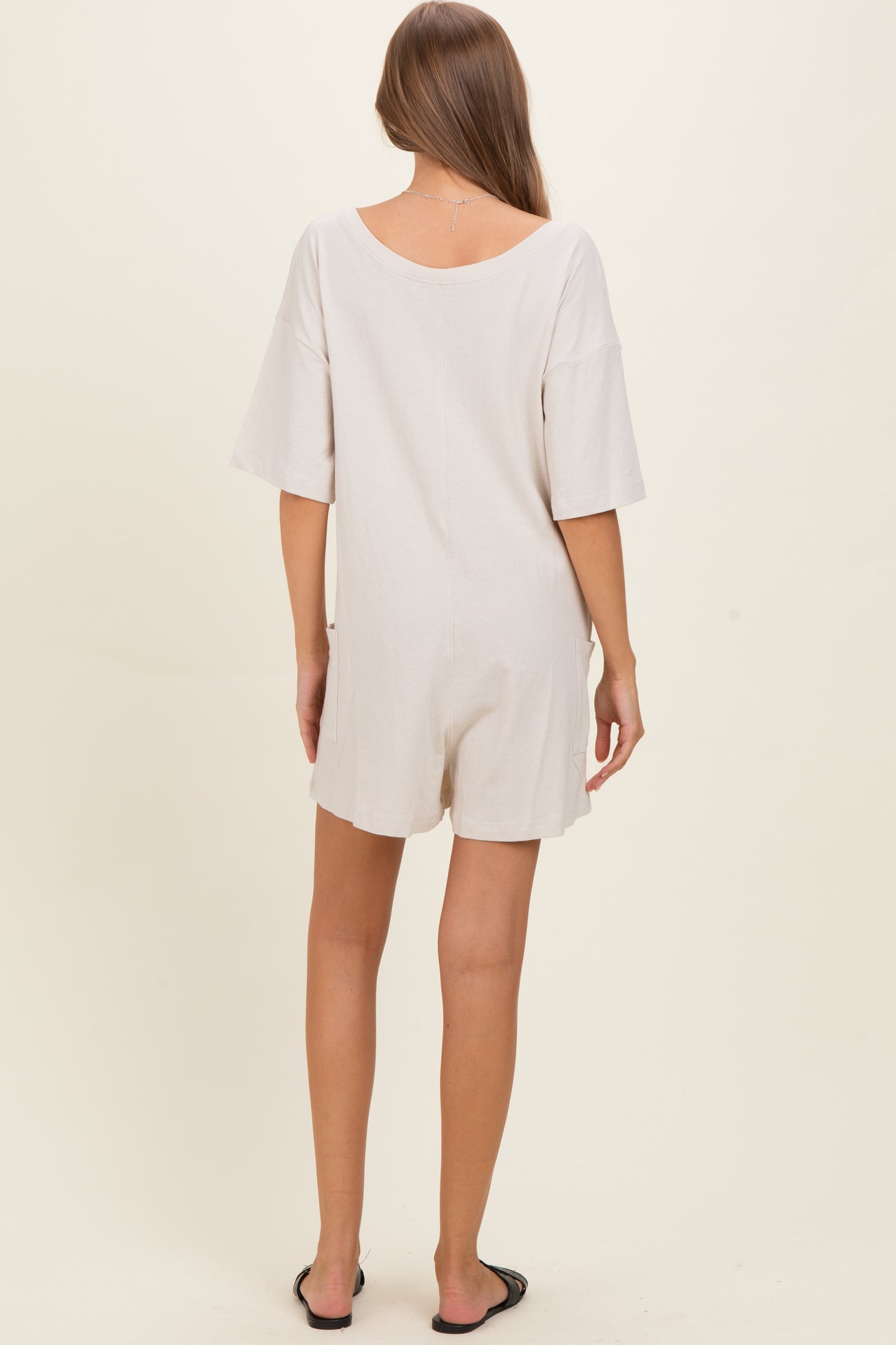 woman wearing a light beige short sleeve maternity romper, showing a relaxed fit and back view