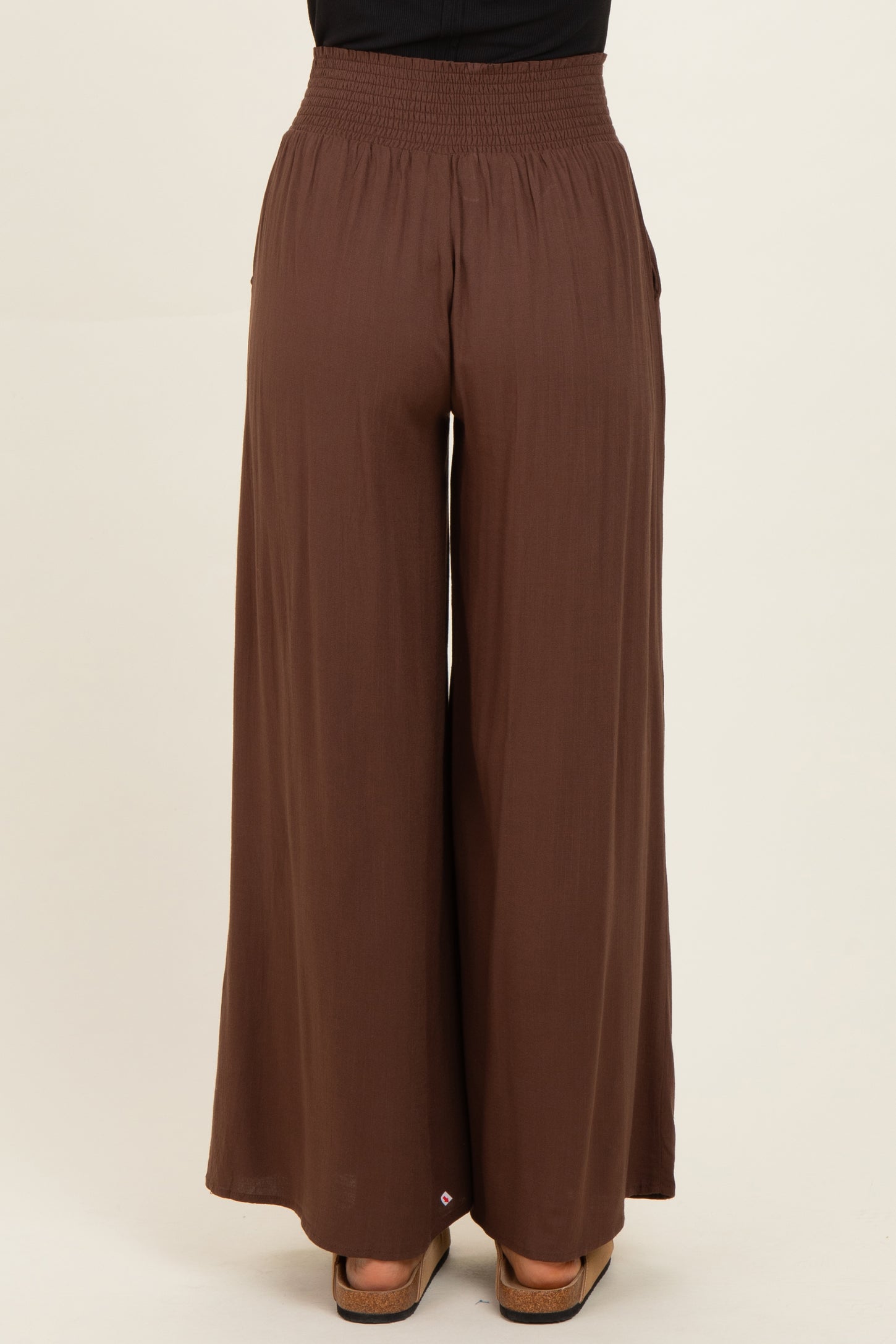 woman wearing brown wide-leg pants with a smocked waistband and side pockets, shown from the back
