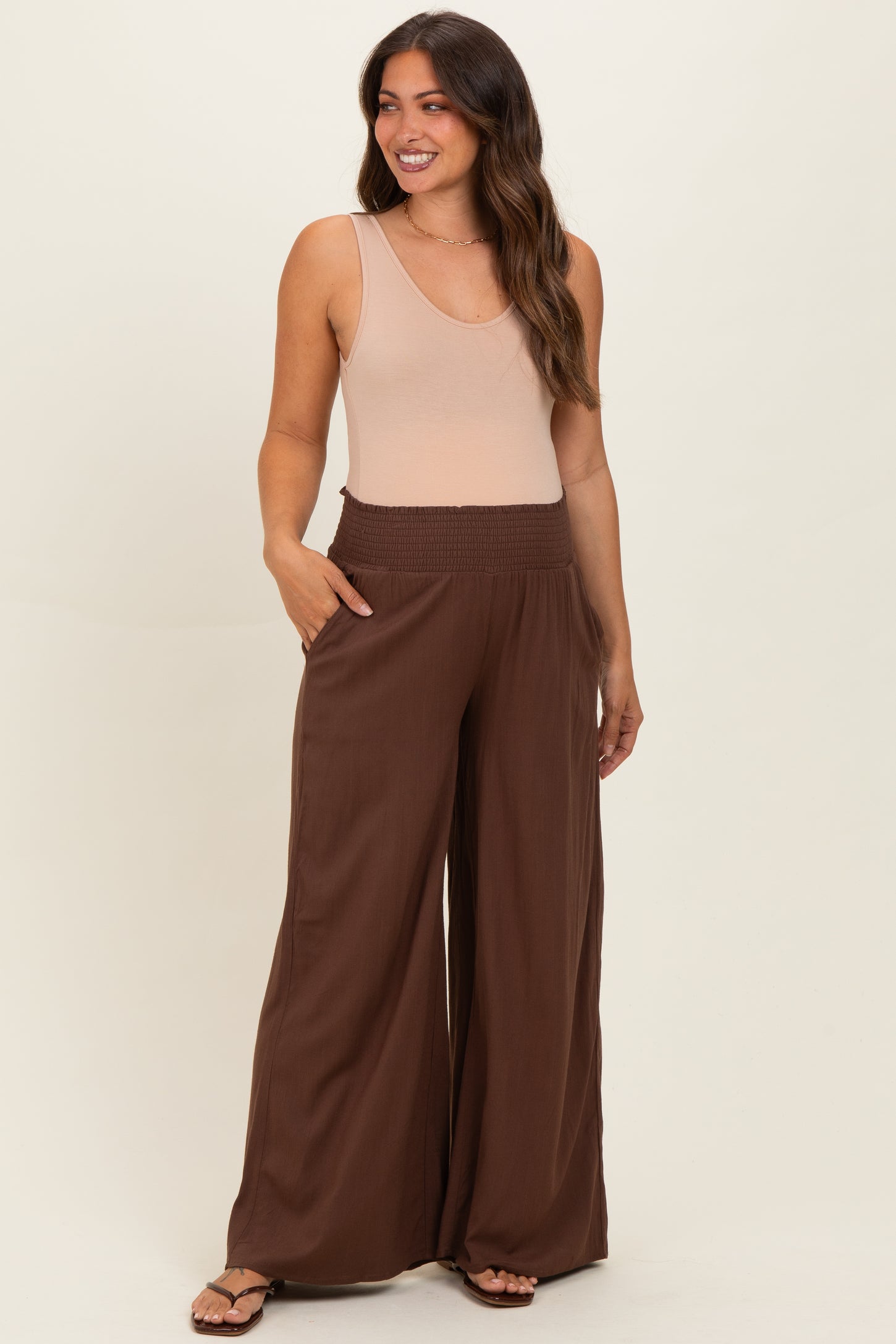 woman wearing a beige tank top and brown wide-leg maternity pants with a smocked waistband and pockets