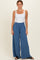 woman wearing a white sleeveless top and blue wide-leg pants with a smocked waistband
