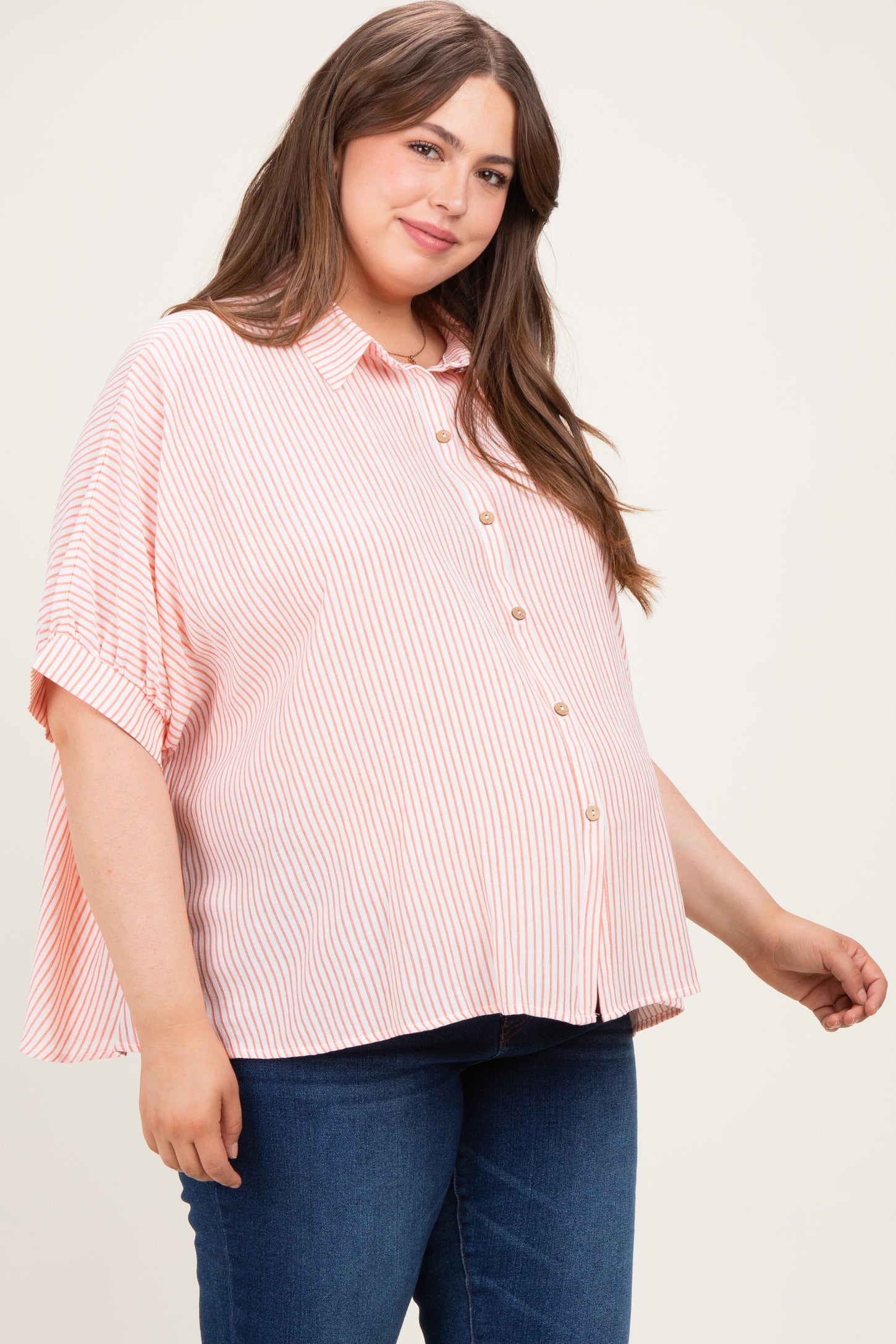 woman wearing a pink and white striped maternity shirt with buttons and a visible baby bump, paired with blue jeans