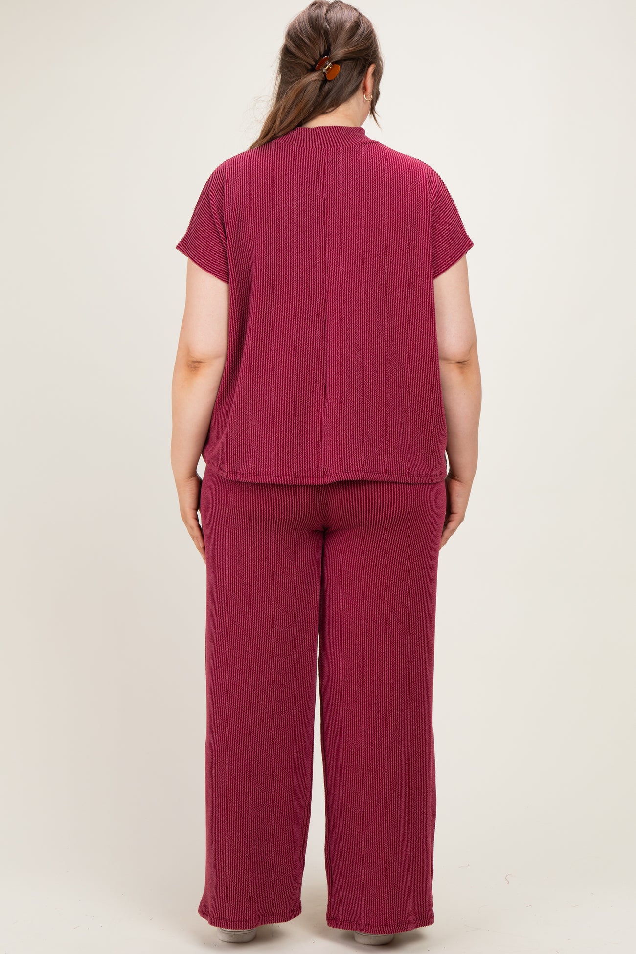 woman wearing a maroon ribbed maternity plus size lounge set, showing the back view with a relaxed fit top and pants