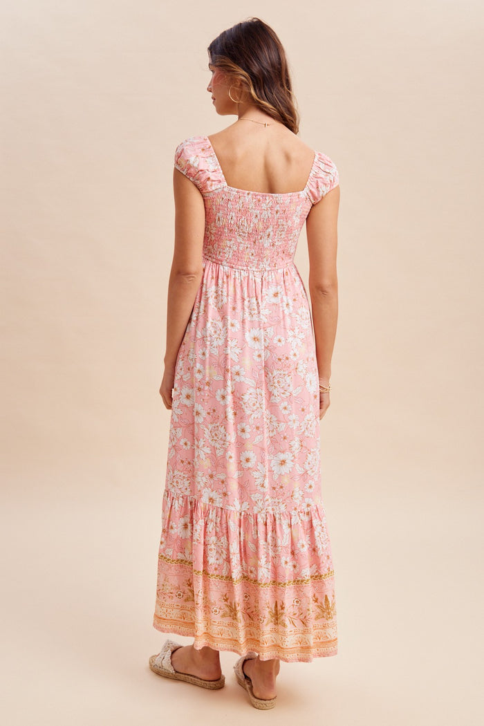 woman wearing a pink floral maxi dress with a square neckline and smocked bodice, showing a tiered skirt from the back