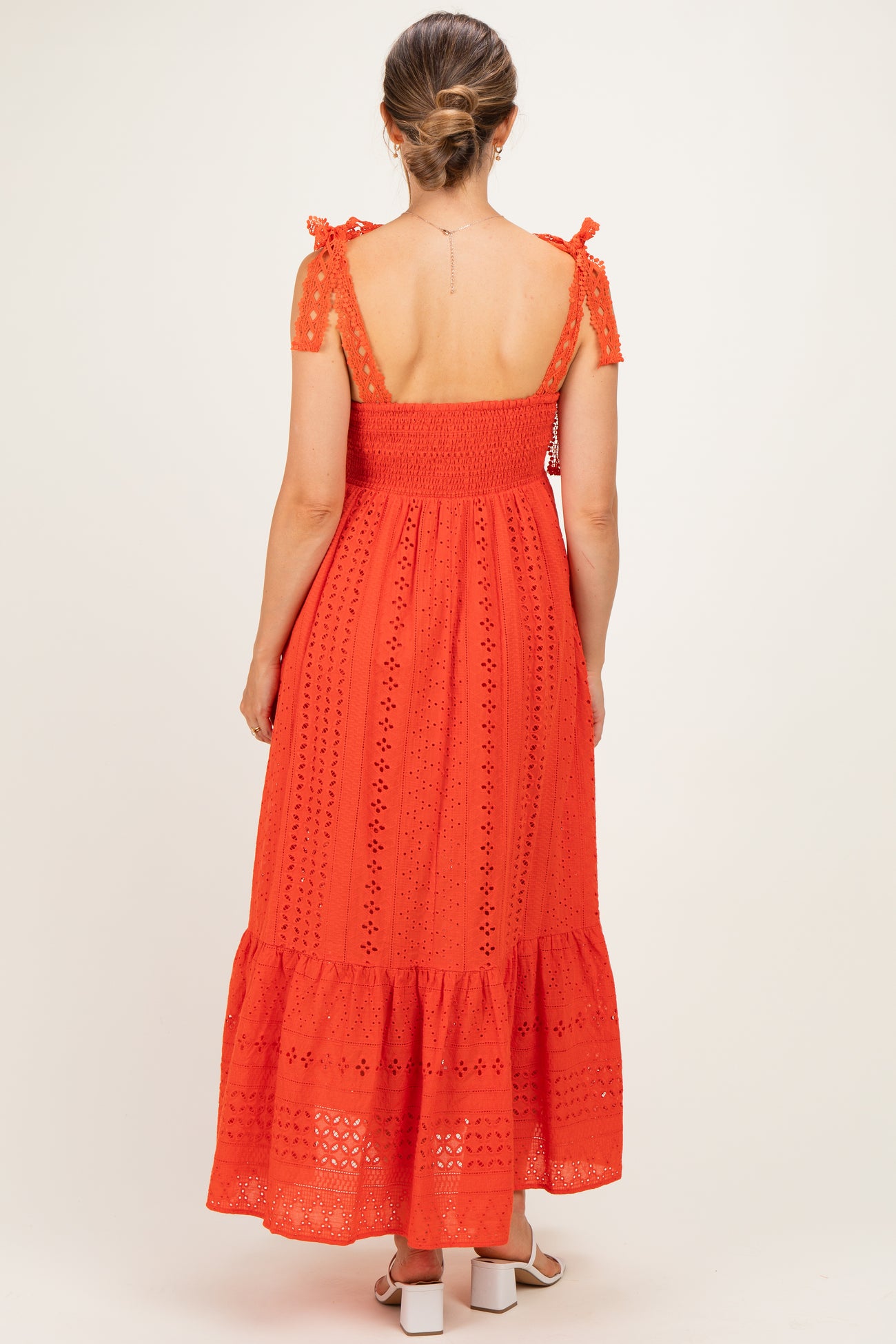 woman wearing a red maternity dress with a smocked bodice, tie shoulder straps, and a tiered skirt