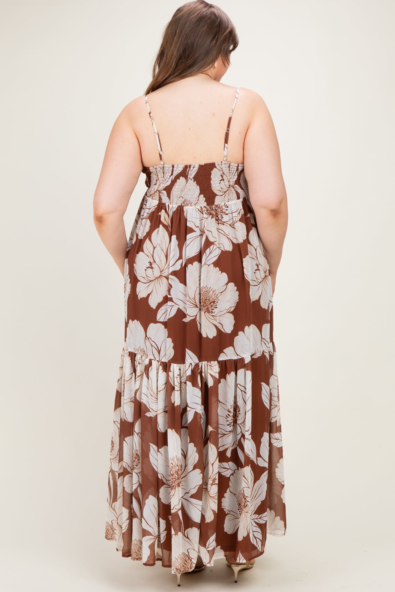woman wearing a brown floral maternity maxi dress, showing the back view with adjustable straps and tiered skirt
