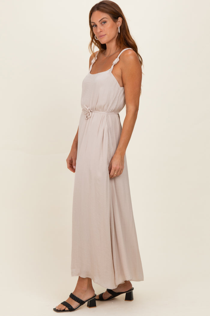 woman wearing a light beige sleeveless maxi dress with a waist tie and ruffled straps