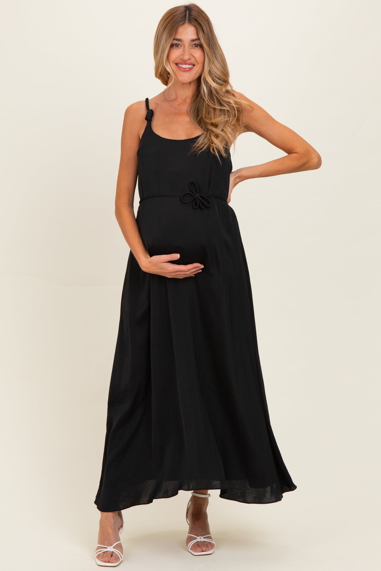 woman wearing a black maxi maternity dress with a bow detail and holding her baby bump