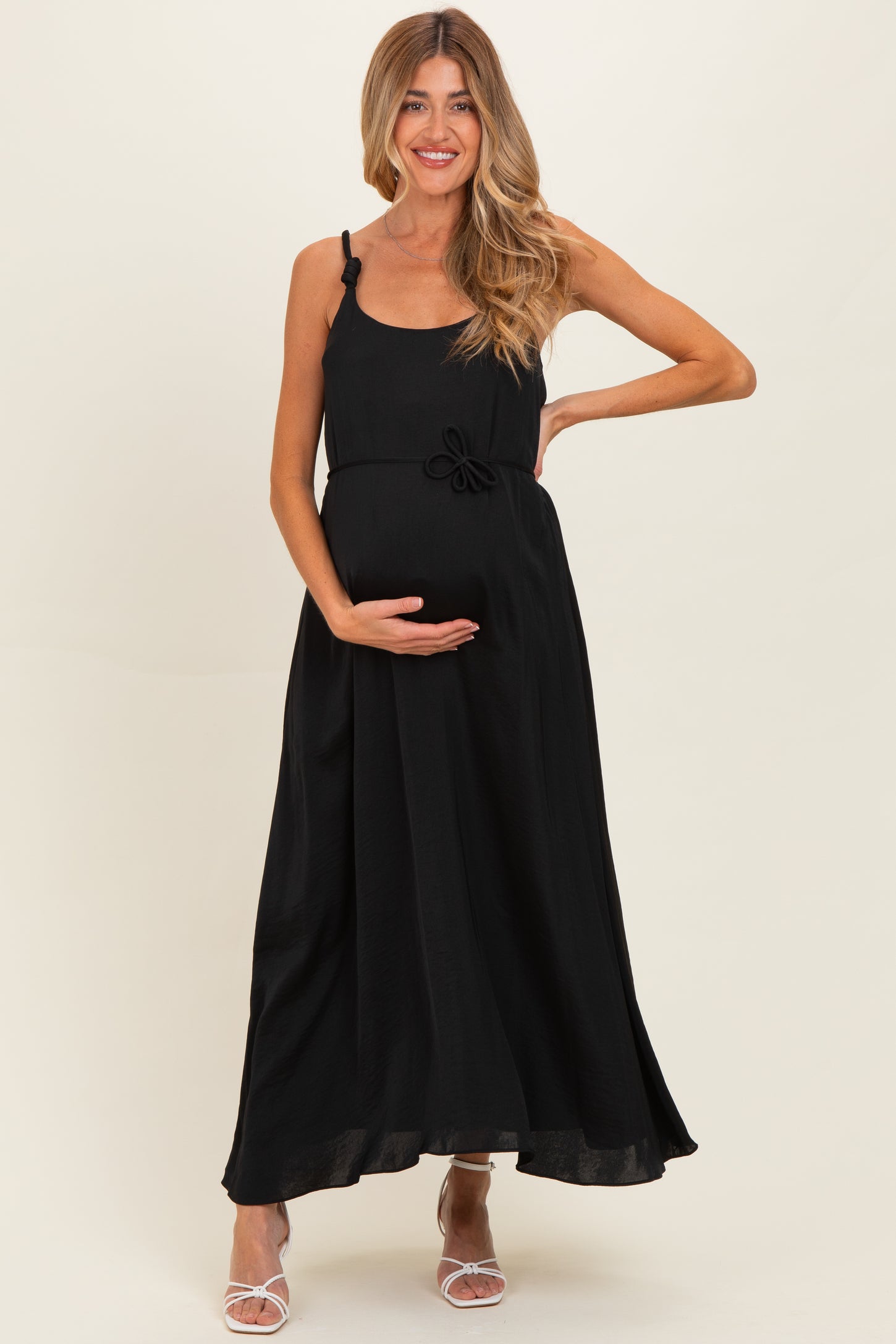 woman wearing a black maxi maternity dress with a bow detail and holding her baby bump
