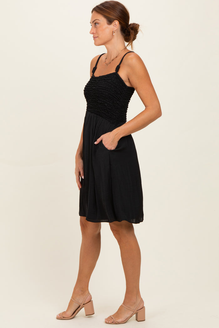 woman wearing a black smocked sundress with adjustable straps and side pockets, paired with beige block heel sandals
