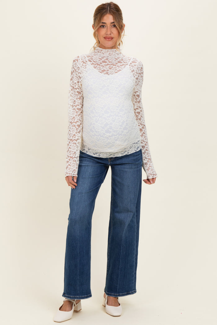 woman wearing a white lace maternity top with long sleeves and blue wide-leg maternity jeans, showcasing her baby bump