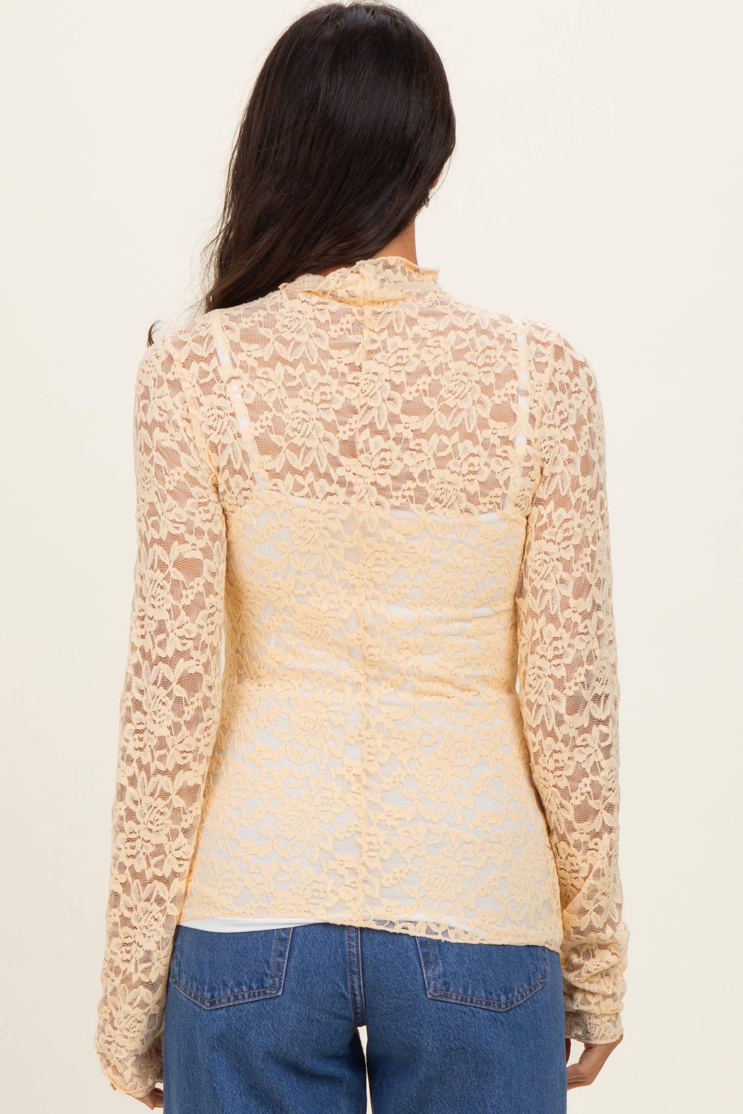 back view of a woman wearing a sheer yellow lace long sleeve top over a fitted bodice with a casual style