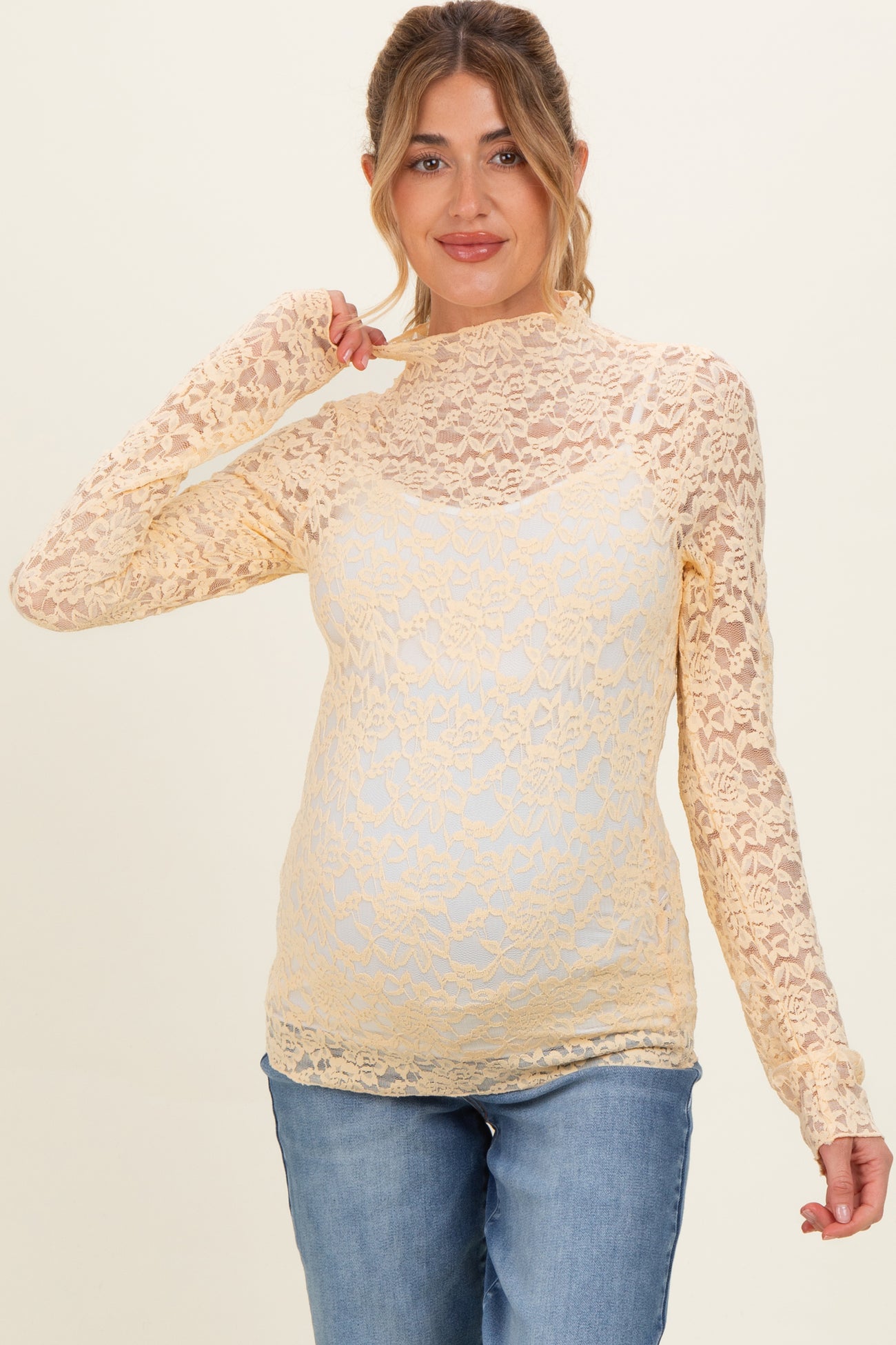 woman wearing a yellow lace long sleeve maternity top and showing her baby bump