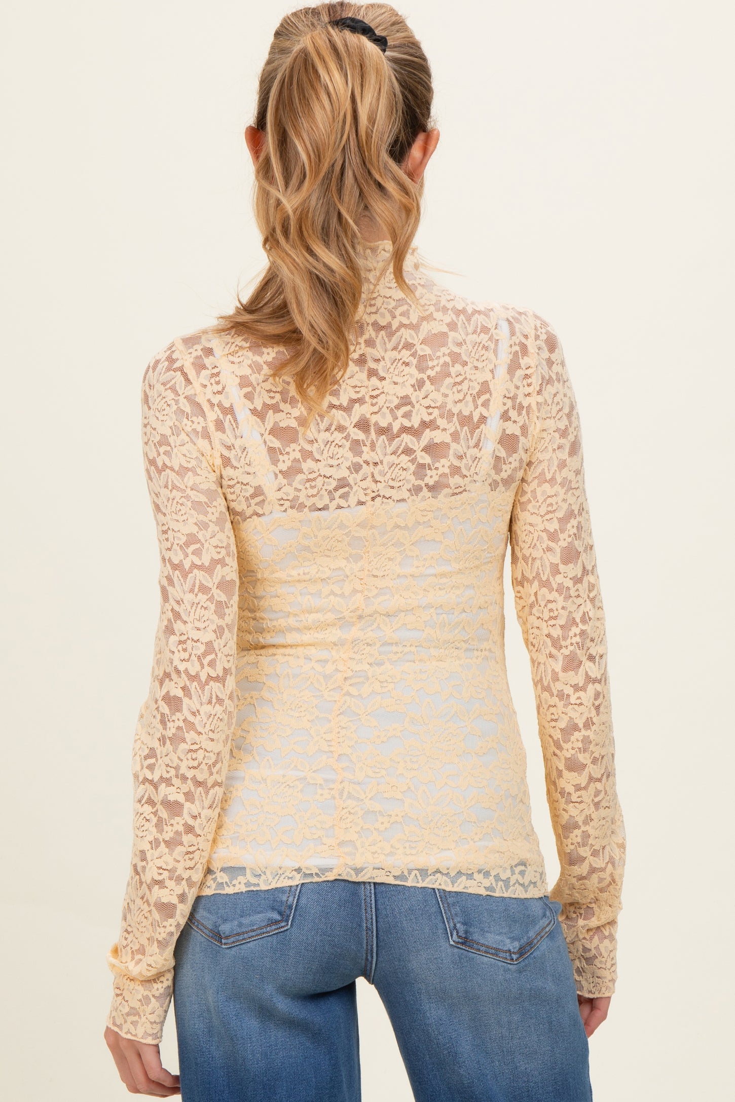 woman wearing a sheer yellow lace maternity top with long sleeves and a fitted silhouette, viewed from the back