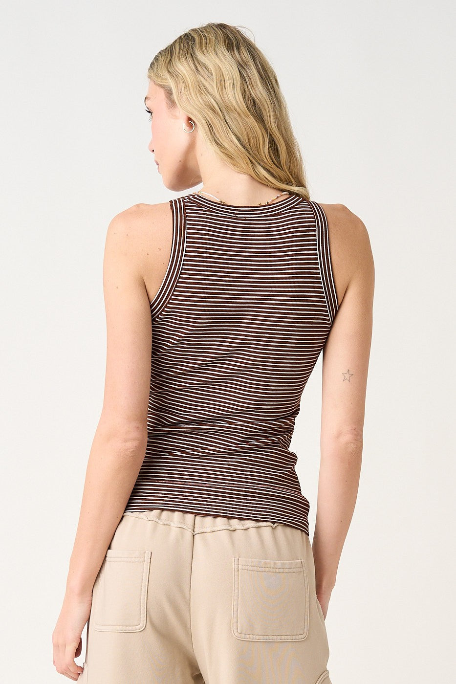 woman wearing a brown and white striped fitted tank top, viewed from the back, paired with beige pants