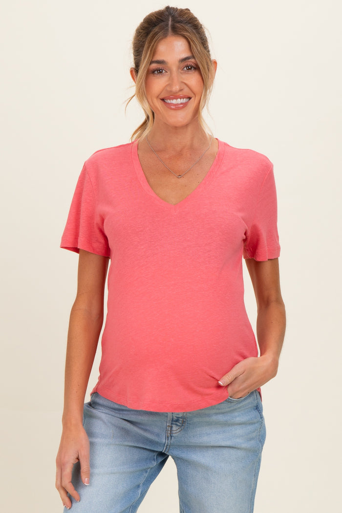 woman wearing a coral v-neck maternity top and showing her baby bump with light wash jeans