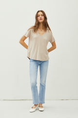 woman wearing a beige v-neck t-shirt with short sleeves and light blue flared jeans, standing on a neutral background