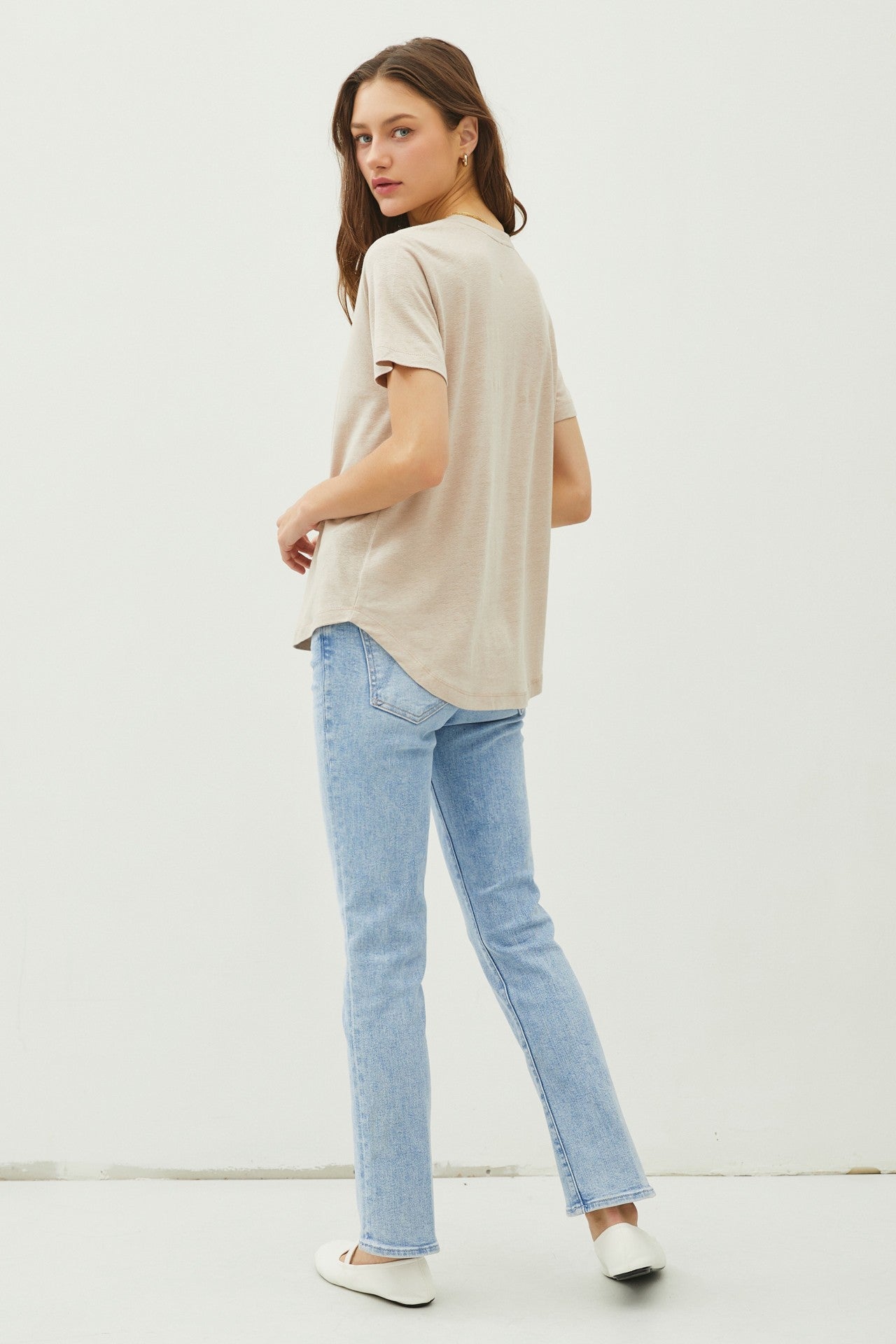 woman wearing a beige t-shirt and light blue straight leg jeans, facing away from the camera