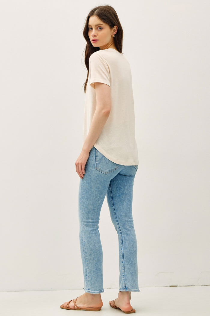 woman wearing a light beige short sleeve t-shirt and light blue skinny jeans, viewed from the back