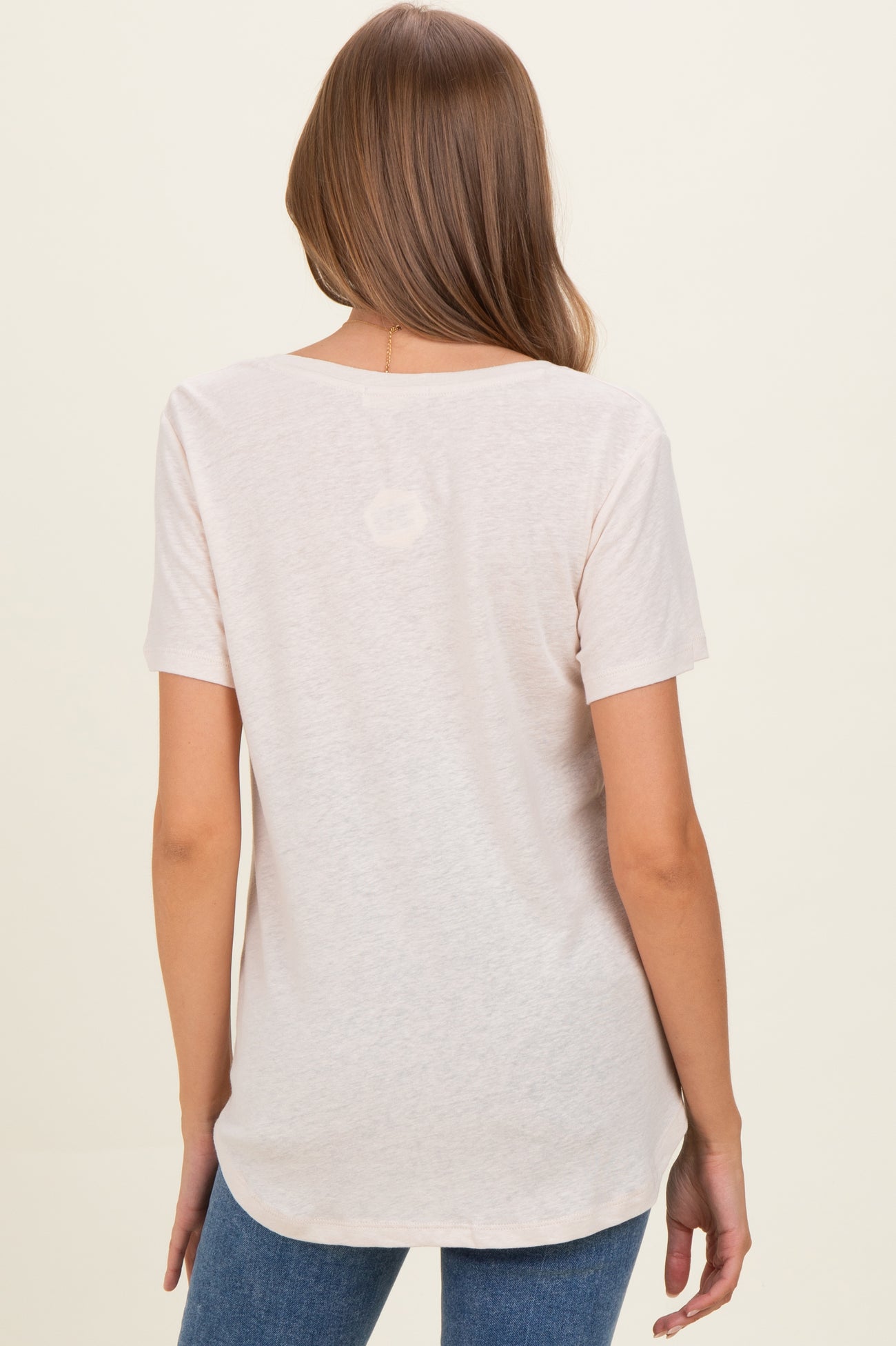 woman wearing a light pink short sleeve maternity top, showing the back and styled with blue jeans