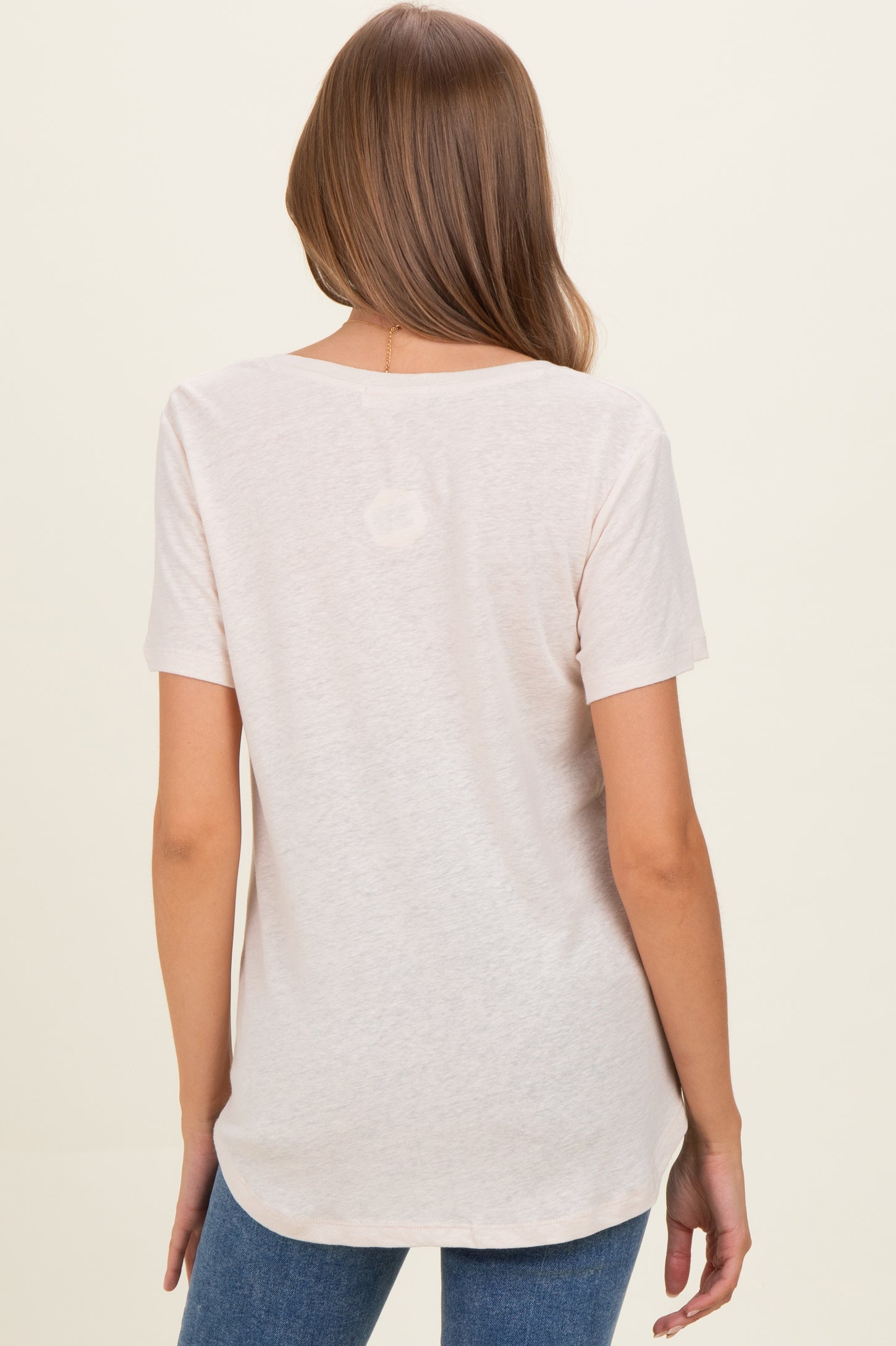 woman wearing a light pink short sleeve maternity top, showing the back and styled with blue jeans
