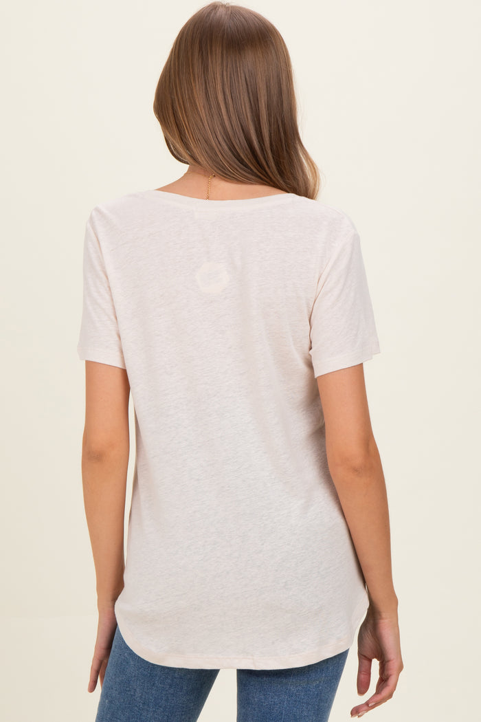 woman wearing a light pink short sleeve maternity top, showing the back and styled with blue jeans