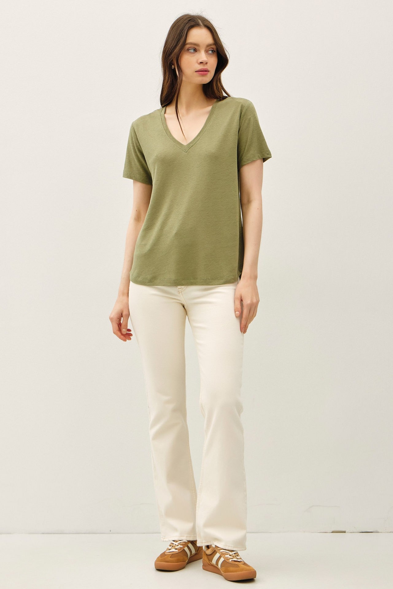 woman wearing a green short sleeve v-neck t-shirt and white flared jeans with brown sneakers