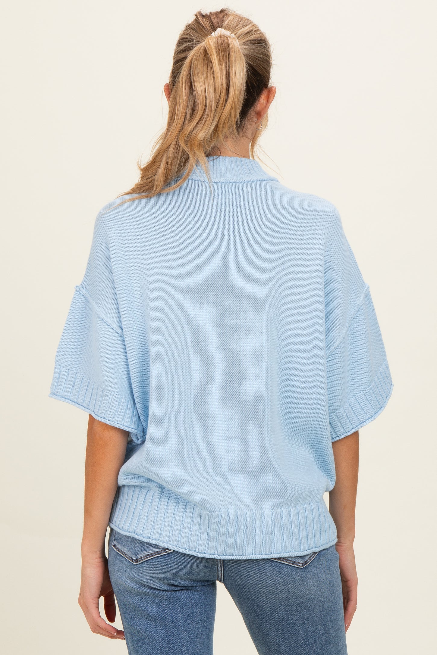 woman wearing a light blue short sleeve maternity sweater, showing a relaxed fit and ribbed hem