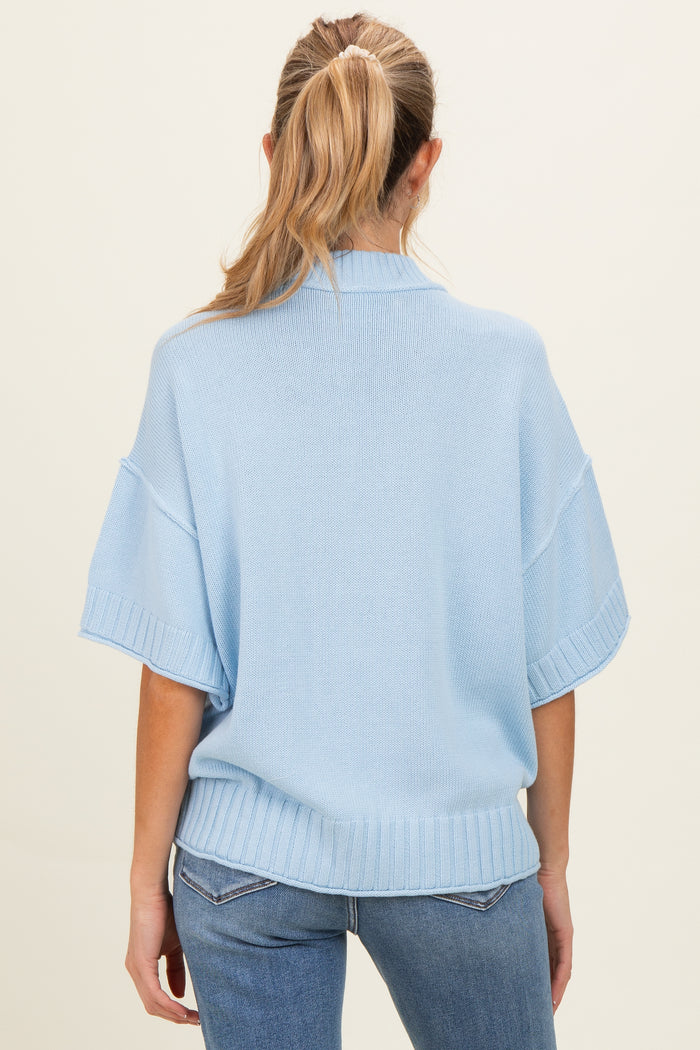 woman wearing a light blue short sleeve maternity sweater, showing a relaxed fit and ribbed hem