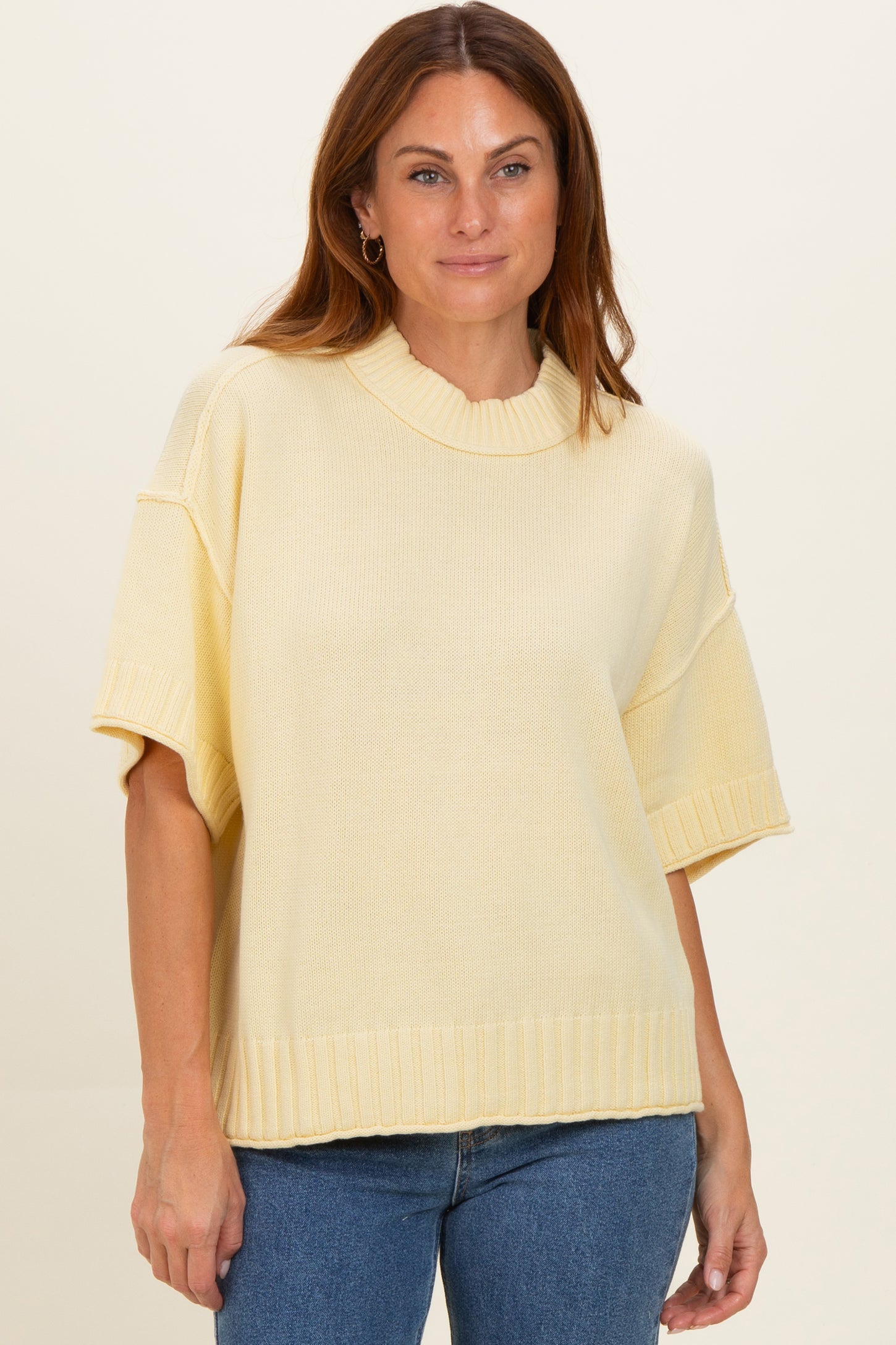 woman wearing a soft yellow oversized sweater with short sleeves and a ribbed neckline, paired with blue jeans