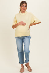 woman wearing a light yellow maternity sweater and blue jeans while holding her baby bump