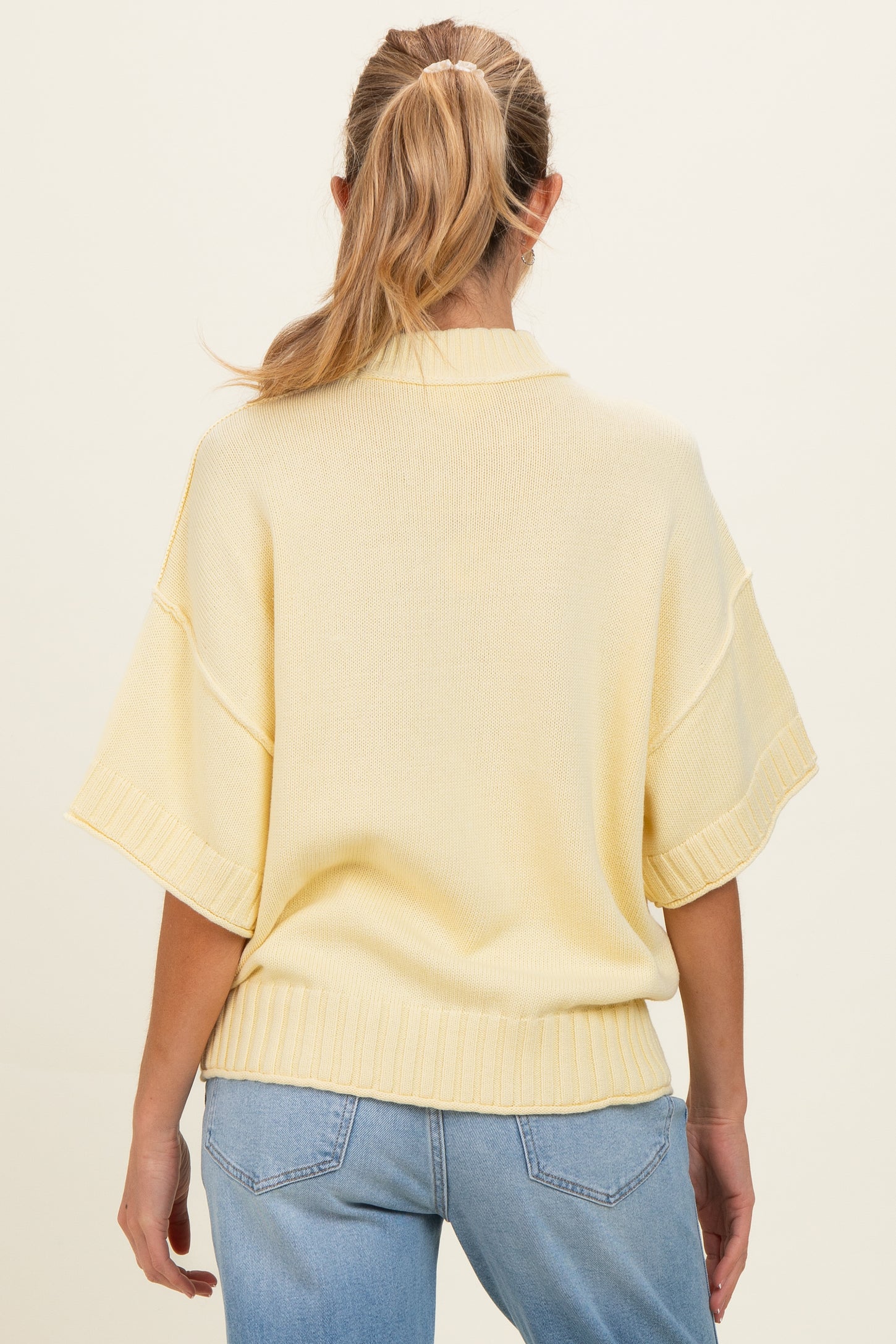 woman wearing a soft yellow oversized maternity sweater with short sleeves and a ribbed hem, seen from the back