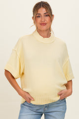 woman wearing a light yellow maternity sweater with a high neckline and short sleeves, showing her baby bump